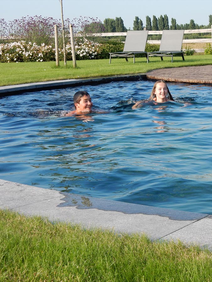 Aanleg zwembad, omzoomd met dallen in blauwsteen, in een landelijke tuin.